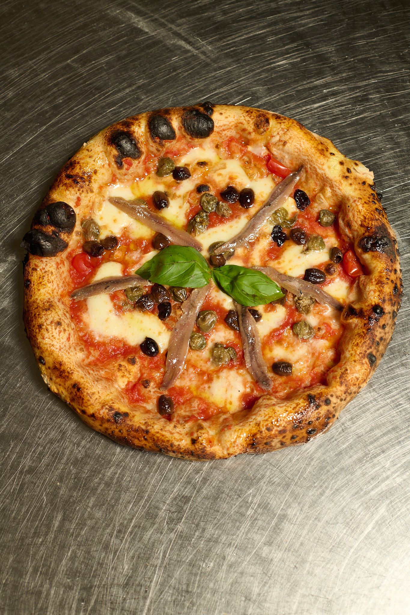 Pizza with anchovies, capers, olives and basil, seen from above